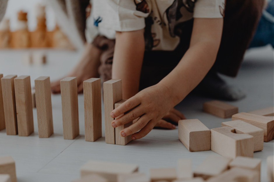 Child playing with wooden blocks while mom supervises, showing the constant demands of parenting that make unmasking harder for neurodivergent mothers