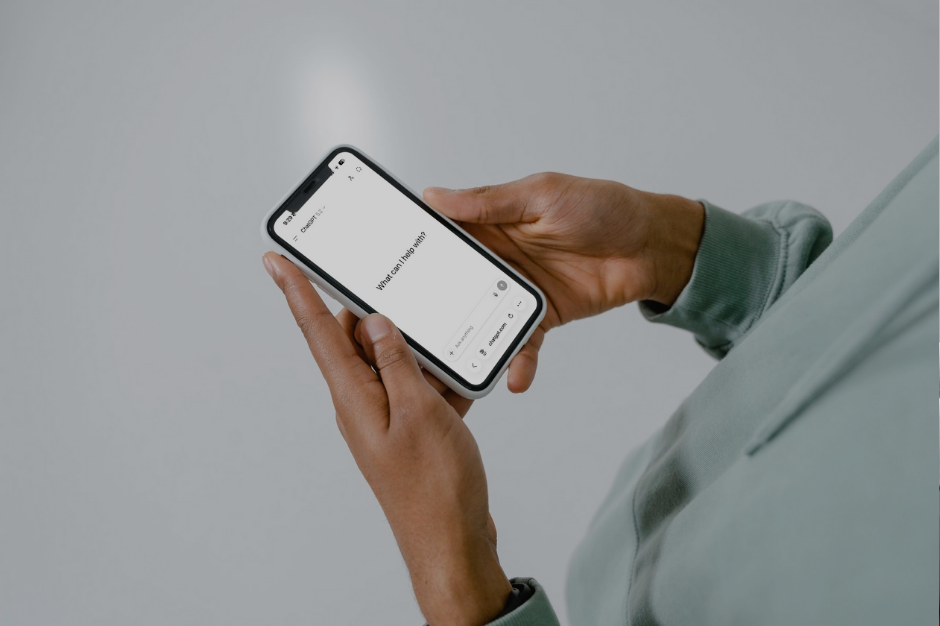 Person in sage green hoodie holding iPhone displaying a help request screen with empty text field and keyboard visible