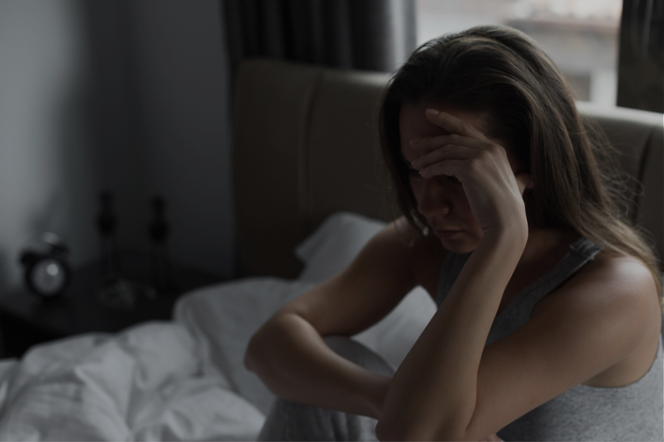 Overwhelmed woman sitting on bed with hand on head illustrating RSD shutdown and emotional overload