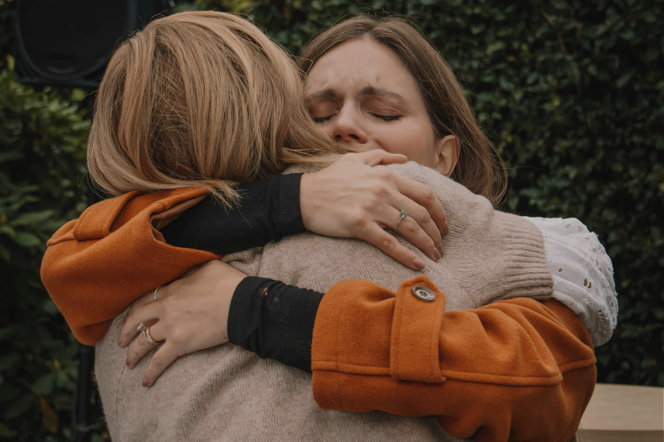 Two women hugging tightly outdoors showing emotional support after a hard conversation