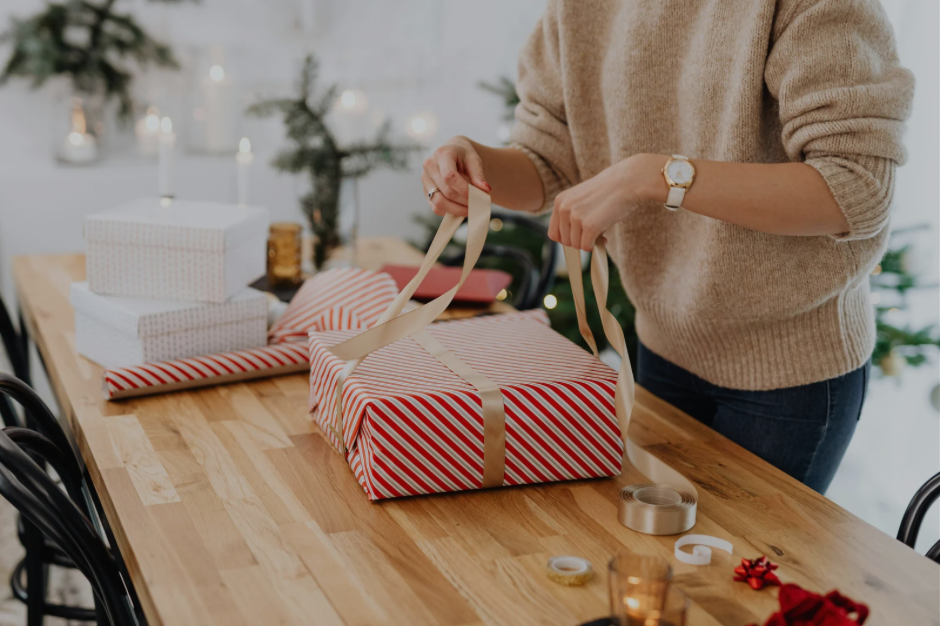 Person wrapping a red and white stripped Christmas present on a wooden table