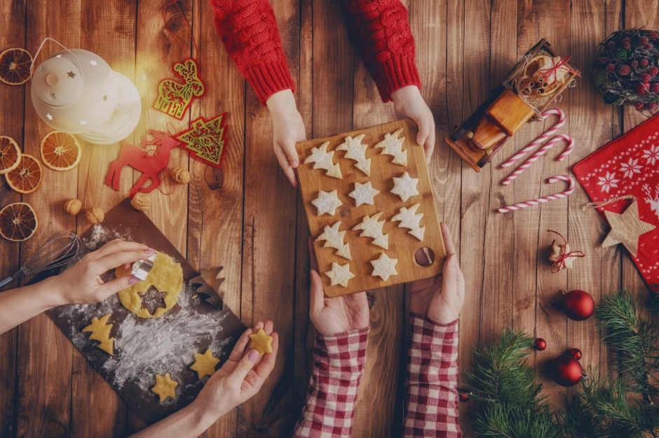 Overhead shot of a family passing Christmas cookies to each other with Christmas decorations strewn across the table