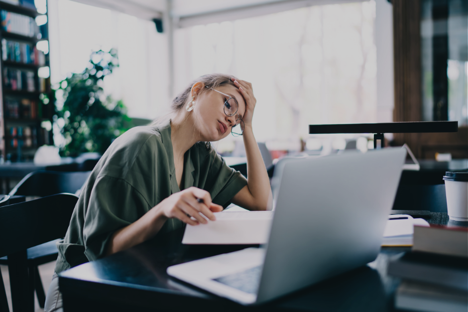 Overwhelmed neurodivergent woman at desk with hand on head, laptop open, capturing the feeling of waking up already overstimulated with conflicting autistic and ADHD needs