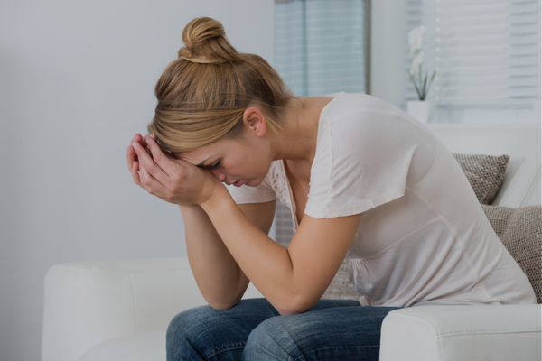 Overwhelmed mother sitting on couch with hands covering her face, experiencing mental load exhaustion